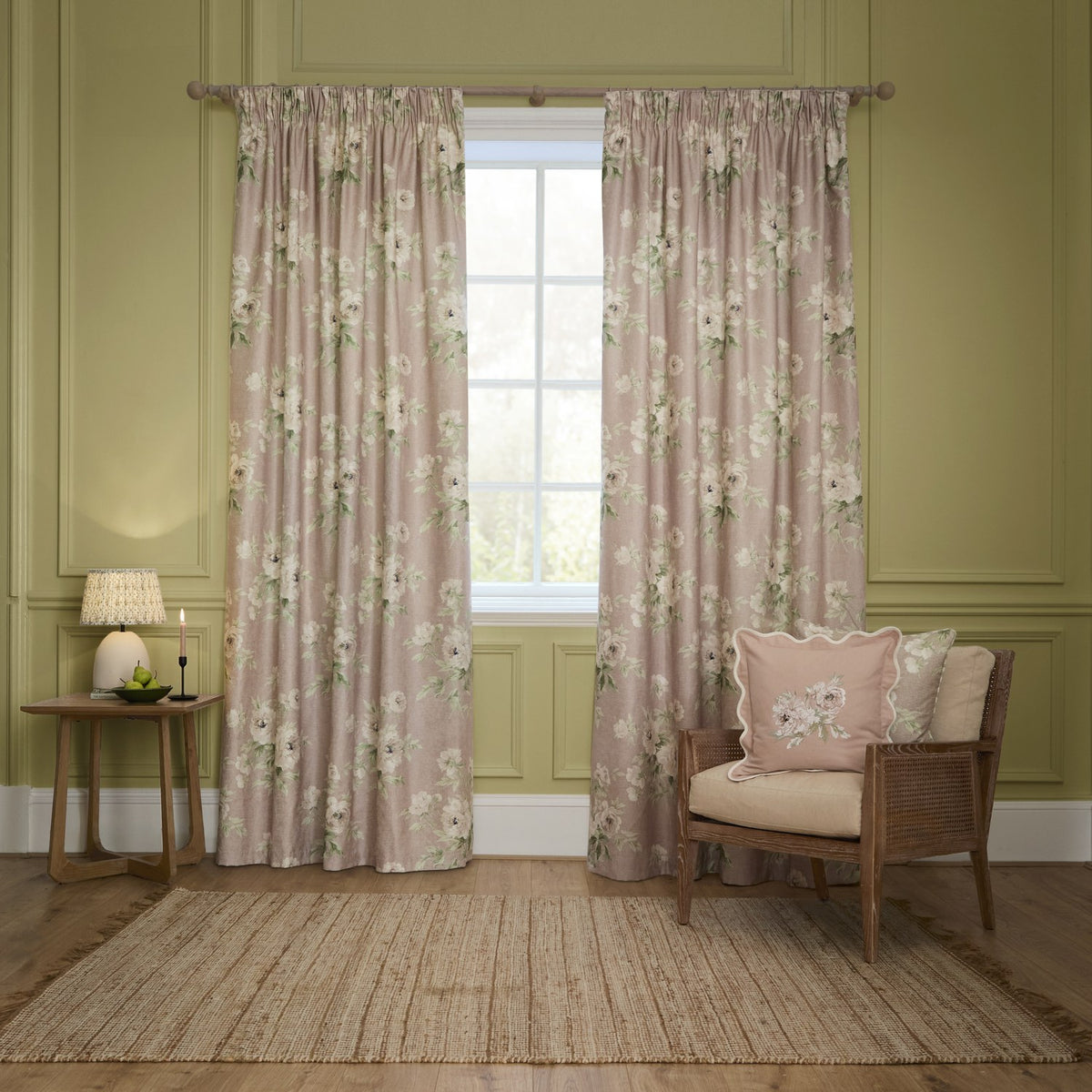 Adele Floral Cotton Cushion in rose-pink with embroidered floral spray and scalloped edge, styled on a wicker armchair in a green-panelled living room.