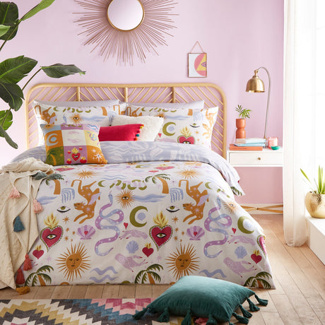 Alchemy Reversible Abstract Duvet Cover Set in multicolour, cream polycotton bedding printed with suns, moons, hearts, snakes and palms, styled on a bed in a pink bedroom.