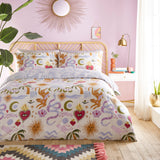 Alchemy Reversible Abstract Duvet Cover Set in Multicolour, styled on a bed in a pink bedroom with cream fabric featuring suns, snakes, hearts, moons and palm motifs, plus matching pillowcases.