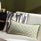 Alexa Reversible Cotton Cushion in olive green with cream basket weave pattern, rectangular bolster shape with fringe trim, styled on a boucle sofa beside a patterned cushion.