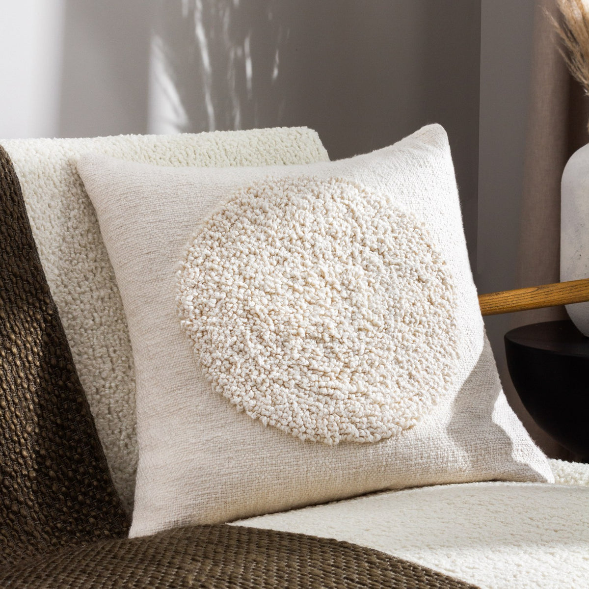 Almo Abstract Cotton Cushion in ecru, woven cotton front with a raised boucle circle motif, styled on a boucle armchair in a living room setting.