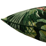 Close-up corner view of the Amazon Creatures Reversible Velvet Cushion in Jade, showing a jungle print of palm fronds and leaves with a green piped edge on a white background.