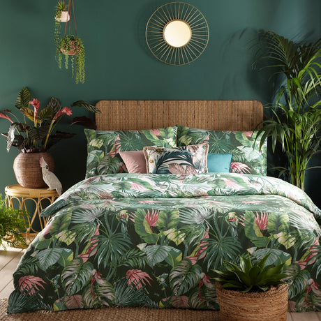 Amazonia Reversible Jungle Duvet Cover Set in Jade, styled on a bed with rattan headboard, featuring green botanical and rainforest animal print with pink accents in a dark green bedroom.