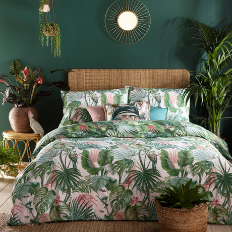 Amazonia Reversible Jungle Duvet Cover Set in Jade, shown white-side up with green and pink botanical print, styled on a bed with rattan headboard and cushions in a tropical-themed bedroom.