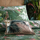 Amazonia Reversible Jungle Duvet Cover Set in Jade, styled on a bed with a matching tropical print cushion, layered pillowcases, and green foliage in the background.