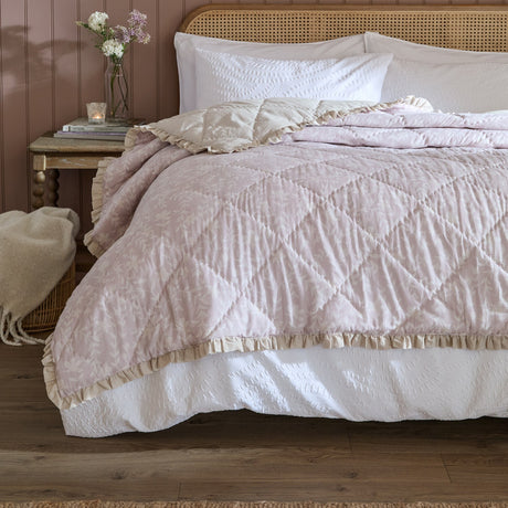Amelia Ditsy Cotton Bedspread in blush, diamond-quilted with a floral sprig print and cream frilled trim, shown on a bed with white patterned pillows in a bedroom setting.