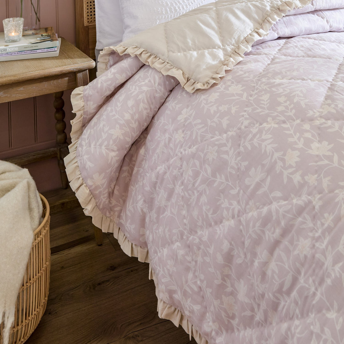 Amelia Ditsy Cotton Bedspread in blush, quilted diamond texture with a ditsy floral print and cream frilled edge, shown on a bed beside a wooden nightstand.