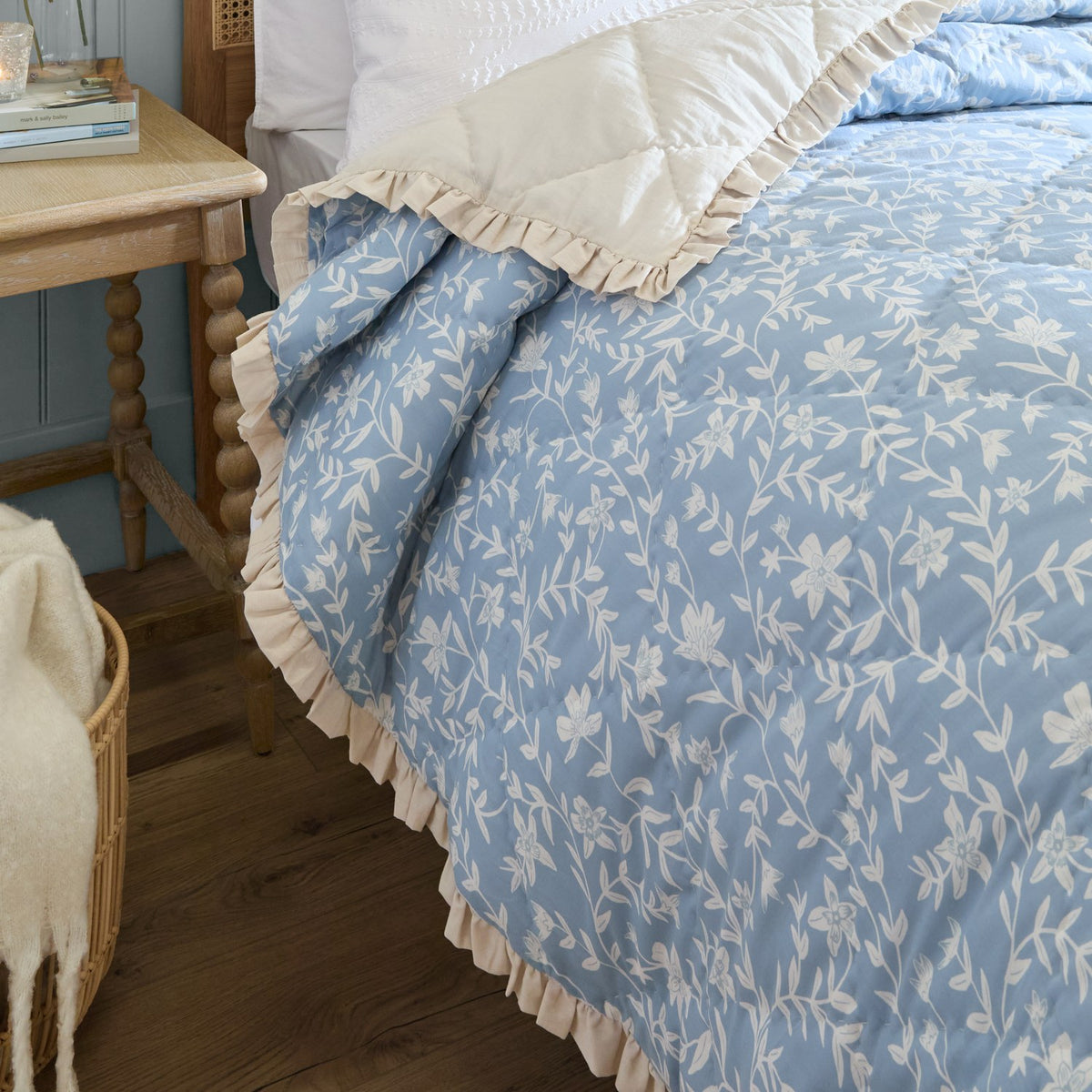 Amelia Ditsy Cotton Bedspread in Delph Blue with white floral print and cream ruffled edge, shown quilted on a bed in a bedroom setting.