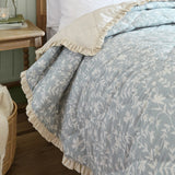 Amelia Ditsy Cotton Bedspread in seafoam, diamond-quilted cotton throw with small floral print and cream ruffled trim, shown folded on a bed in a bedroom setting.