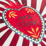Close-up of the Amor Eterno velvet cushion showing a hand-painted red sacred heart with "Amor Eterno" text, orange leaf motifs, grey scalloped trim, and red-white sunburst rays.