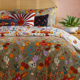 Amor Eterno Abstract Velvet Cushion in red, styled on a bed with a flaming sacred heart motif and red-and-white radiating rays, shown among patterned bedding and cushions.