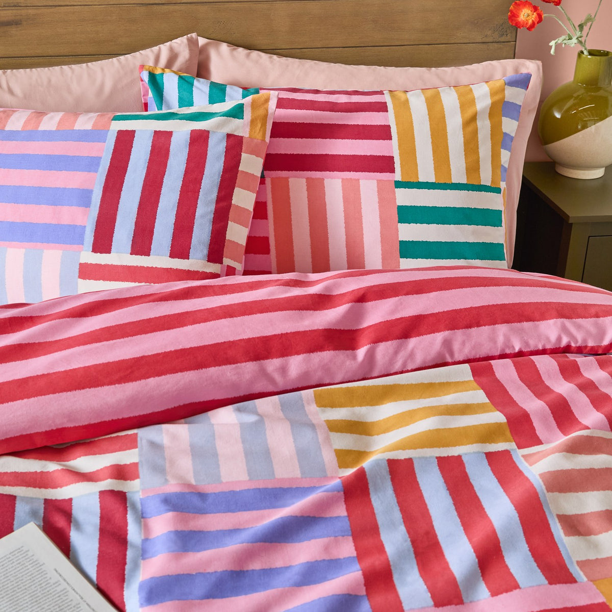 Ana Stripe Reversible Duvet Cover Set on a bed, showing the patchwork striped side in pink, red, teal, lilac and yellow with matching pillowcases in a bedroom setting.