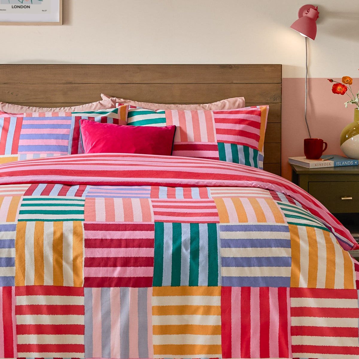 Ana Stripe Reversible Geometric Duvet Cover Set in Multi, on a bed with pink, red, teal and orange patchwork squares, striped pillowcases and a pink velvet cushion.