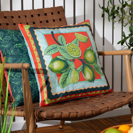 Anemone Reversible Polyester Cushion in Multi, 45 x 45cm, shown outdoors on a woven chair with a printed lime branch design on coral, framed by a teal, peach and gold scalloped border.
