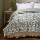 Annabelle reversible cotton bedspread in blue on a bed, showing a floral pattern with a striped border, styled in a bedroom with white ruffled pillows.