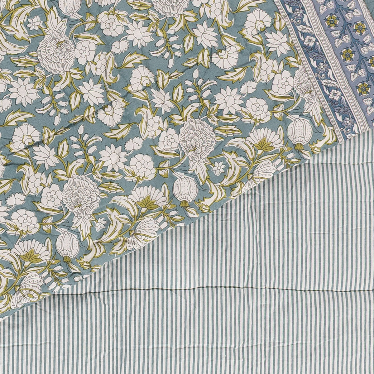Annabelle Reversible Cotton Bedspread in blue, corner turned back to show a scrolling floral design in blue-green and teal beside the matching narrow striped reverse.