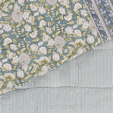 Annabelle Reversible Cotton Bedspread in blue, corner turned back to show a scrolling floral design in blue-green and teal beside the matching narrow striped reverse.