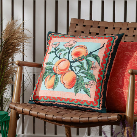 Anemone Reversible Polyester Cushion in multi, square scatter cushion with peach branch and blossom print in coral, green and duck-egg, styled on a woven leather chair.