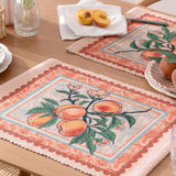 Anemone Floral Polyester Placemats in multicolour, rectangular woven mats with a peach branch print and orange floral border, shown styled on a wooden dining table with fresh peaches.