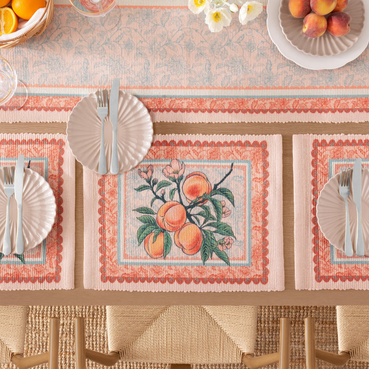 Rectangular polyester placemats with a peach branch print and Jacobean-style floral border in orange, green and pale blue, set on a dining table with plates and cutlery.