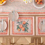 Rectangular polyester placemats with a peach branch print and Jacobean-style floral border in orange, green and pale blue, set on a dining table with plates and cutlery.