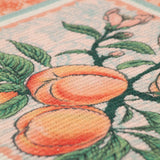 Close-up of an Anemone Floral polyester placemat showing peaches on a branch with green leaves and pink buds, bordered by a pale blue and orange Jacobean-style pattern.