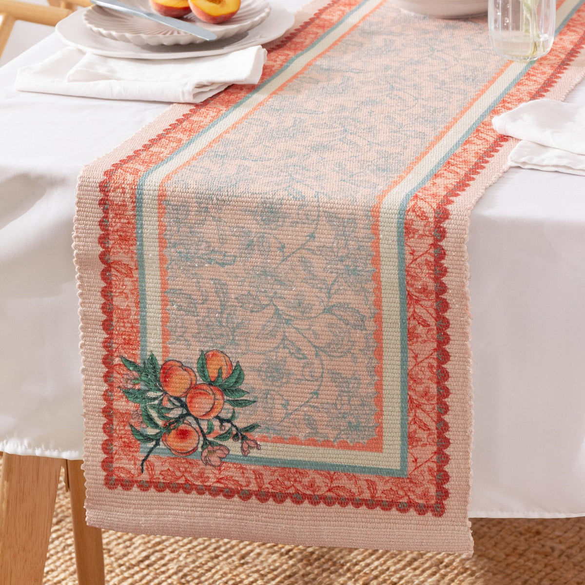 Anemone Floral Polyester Table Runner in multicolour, draped over a dining table with a scalloped coral and terracotta border, botanical ground pattern, and a peach branch motif at the end.