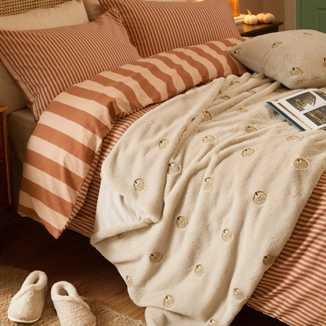Autumn Pumpkins Velvet Faux Fur Throw in natural beige, draped over a bed with embroidered pumpkin motifs, styled with striped bedding and cream cushions.