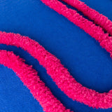 Close-up of the Archie Abstract Cotton Blend Cushion in Cobalt/Pink, showing hand-tufted raised pink pile lines against a smooth woven cobalt blue ground.