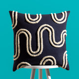 Archie Abstract Cotton Blend Cushion in Mono, a 45 x 45cm square cushion with tufted cream abstract swirl and arch patterns on a black cotton blend cover, shown on a stool against a teal background.