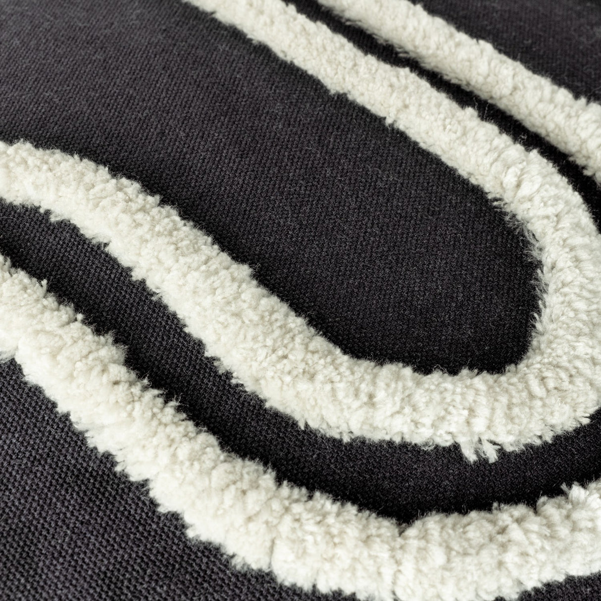 Close-up of the Archie Abstract Cotton Blend Cushion in Mono, showing tufted off-white looped patterns raised against a deep black woven cushion surface.
