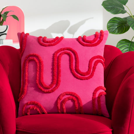 Archie Abstract Cotton Blend Cushion in pink, 45x45cm square with tufted red looping abstract pattern, shown on a red velvet armchair.