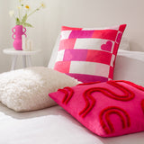 Archie Abstract Cotton Blend Cushion in pink with red tufted looping design, styled on a bed alongside a pink and white checked heart-print cushion and cream faux fur cushion.