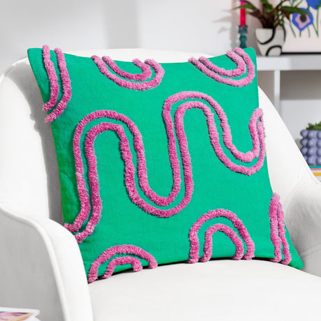Archie Abstract Cotton Blend Cushion in green, with a hand-tufted pink abstract line pattern, shown on a white armchair in a living room setting.