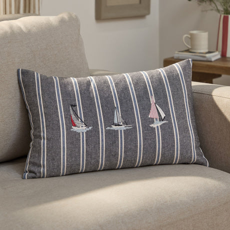 Abersoch Regatta rectangular cushion in navy striped cotton with cream and blue lines, featuring three embroidered sailboats, shown on a beige sofa.