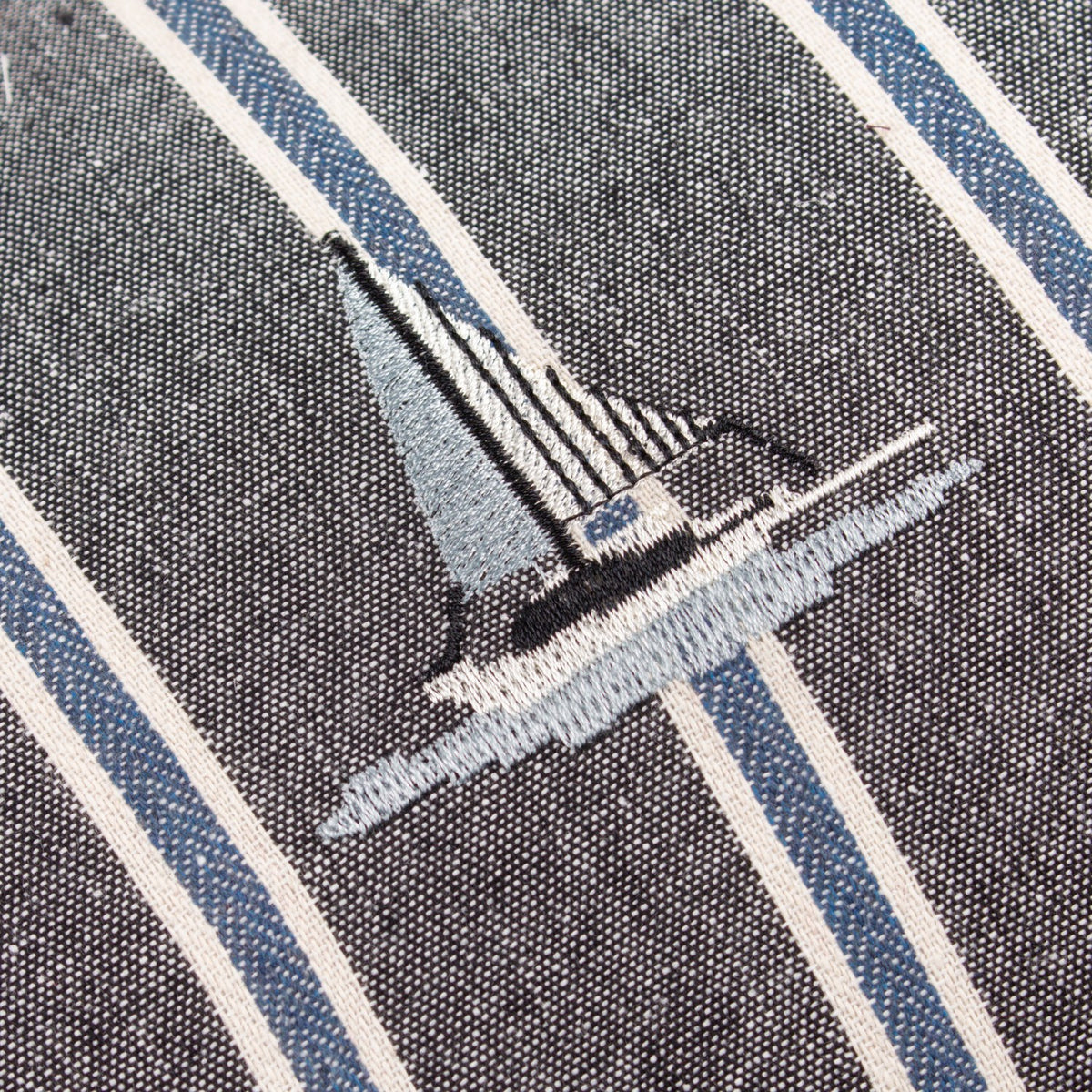 Close-up of the Abersoch Regatta cushion in navy, showing an embroidered sailboat in grey and cream thread on cotton fabric with cream and blue vertical stripes.