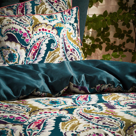 Aretha Cotton Floral Duvet Cover Set in Teal/Olive, showing a paisley print pillowcase and duvet folded back to reveal the plain teal reverse, styled on a bed.
