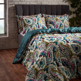 Aretha Cotton Floral Duvet Cover Set in teal and olive, showing a bold paisley print with plum, pink and ivory tones and matching pillowcases on a bed with dark grey headboard.