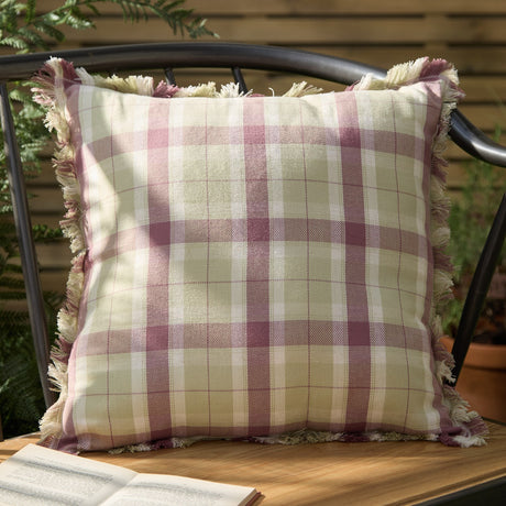 Arrochar Check Linen Cushion in Elderberry, a square cushion with woven tartan check in cream, green and pink tones and a self-fringed edge trim, shown outdoors on a metal garden chair.