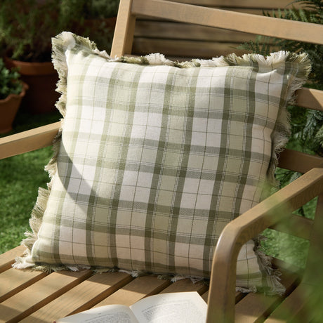 Arrochar Check Linen Cushion in moss green and cream woven tartan with fringed edges, styled on an outdoor wooden chair.
