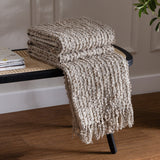Arvo Plain Cotton Throw in feather grey, folded and draped over a black cane bench, showing ridged boucle texture and fringed edge.