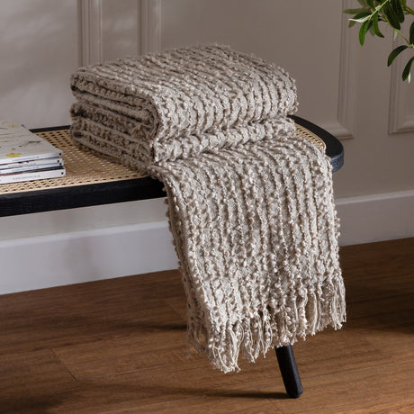 Arvo Plain Cotton Throw in feather grey, folded and draped over a black cane bench, showing ridged boucle texture and fringed edge.