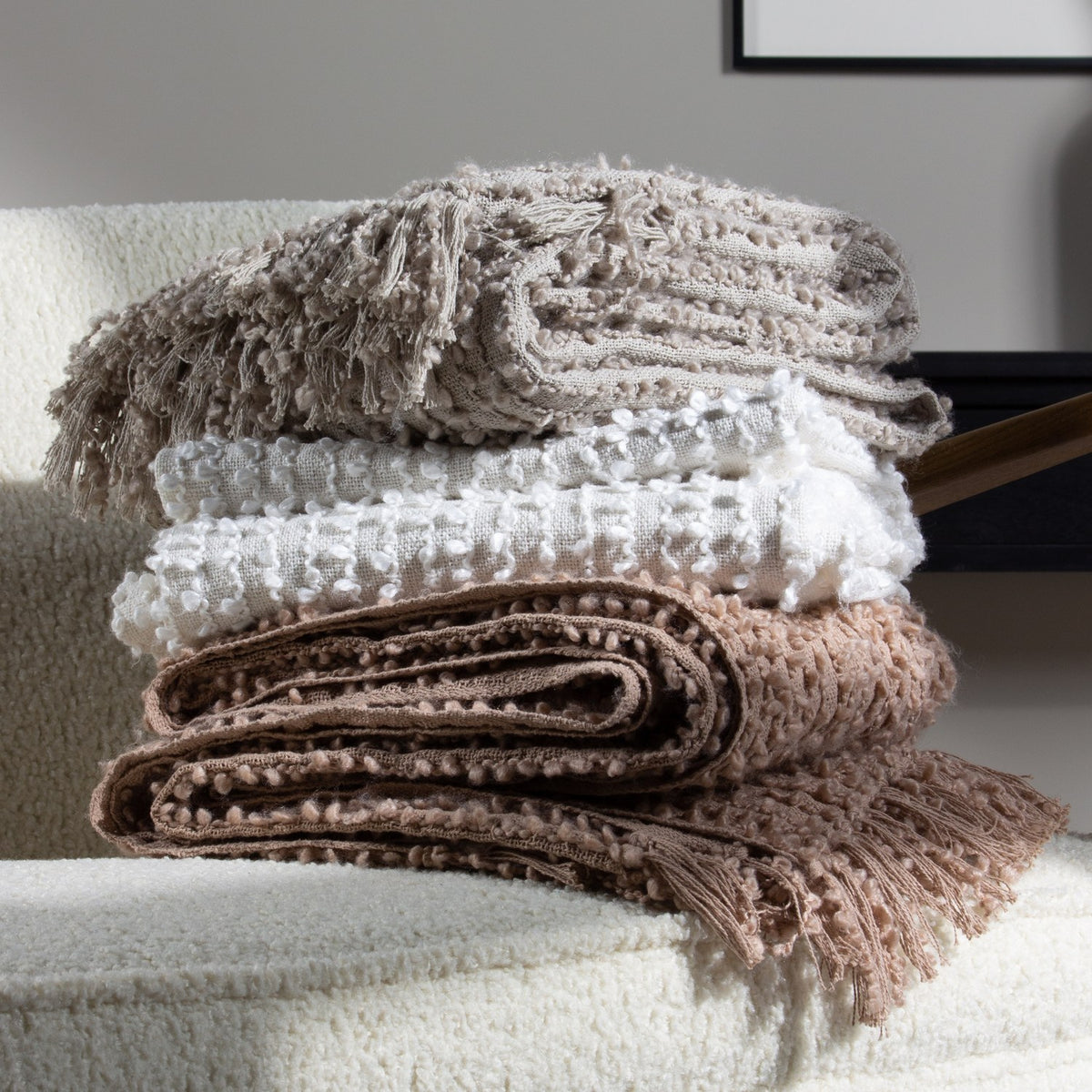 Arvo Plain Cotton Throw in feather grey, folded with textured boucle rows, stacked with other throws on a boucle armchair in a living room setting.