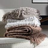 Arvo Plain Cotton Throw in feather grey, folded with textured boucle rows, stacked with other throws on a boucle armchair in a living room setting.