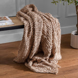 Arvo Plain Cotton Throw in Plaster draped over a bench with fringed edge and boucle-textured ridges, shown in a living room with a plant and wooden floor.