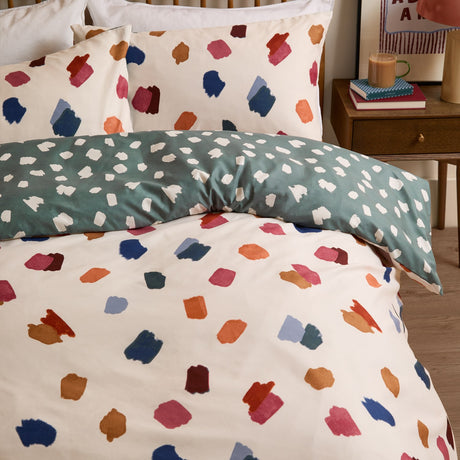 Astrid Abstract Duvet Cover Set on a bed, cream ground with multicoloured hand-painted brushstroke spots, reversing to teal green with cream marks, polyester fabric, styled bedroom setting.