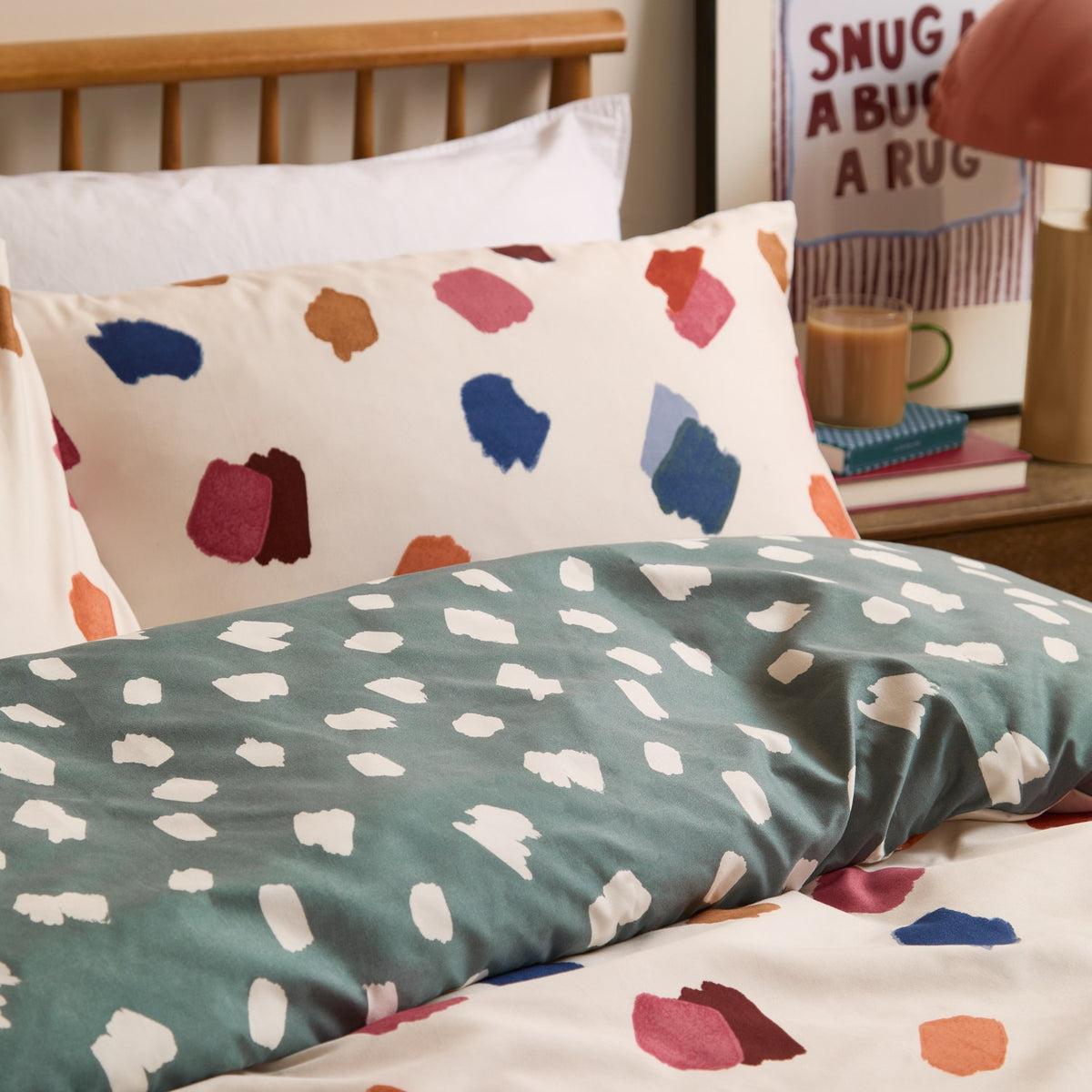 Astrid Abstract Duvet Cover Set on a bed, showing the reversible design with multicoloured brushstroke spots on cream and matching cream-spotted teal green side, styled with a coordinating pillowcase.