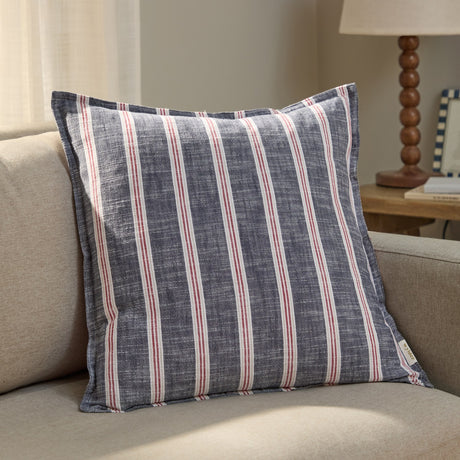 Abersoch Stripe Yarn-Dyed Cotton Cushion in Regatta Red, with red and cream vertical stripes on an indigo-blue cotton ground, shown propped on a beige sofa.