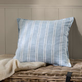 Abersoch Stripe Yarn-Dyed Cotton Cushion in Sail Blue with woven white stripes, shown on a wicker basket beside a cream throw against a panelled wall.