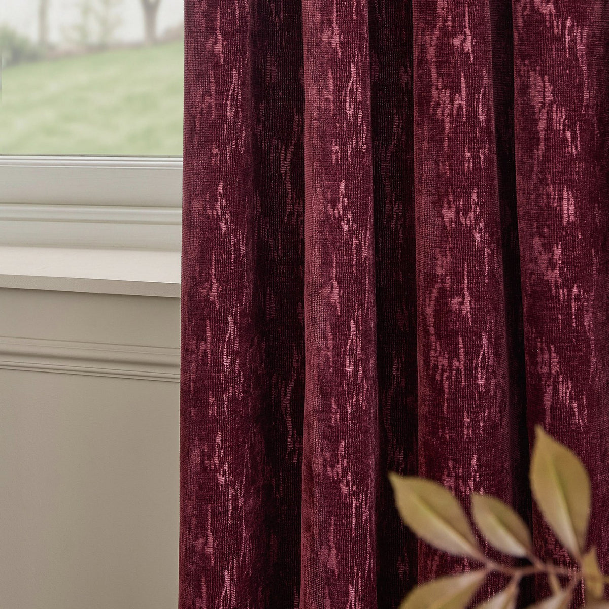 Aurelio Chenille Jacquard Fully Lined Eyelet Curtains in burgundy, shown in soft folds by a window, with a mottled woven texture and abstract pattern.